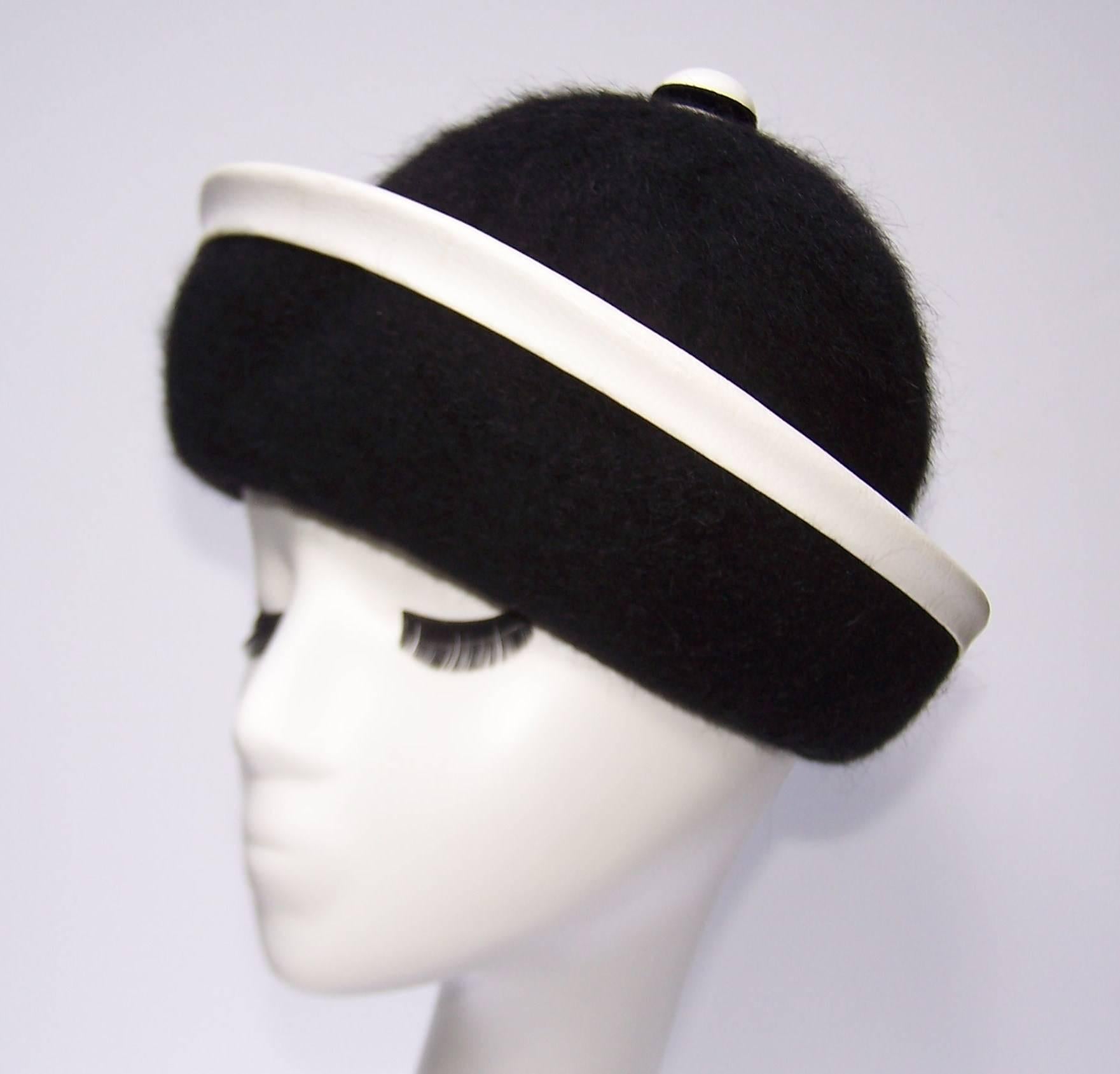 The graphic black and white design of this Henry Pollak hat epitomizes the mod style of the 1960's era.  The shape and style is reminiscent of a classic derby hat with a black mohair body and white leather trim at the brim.  The large white leather