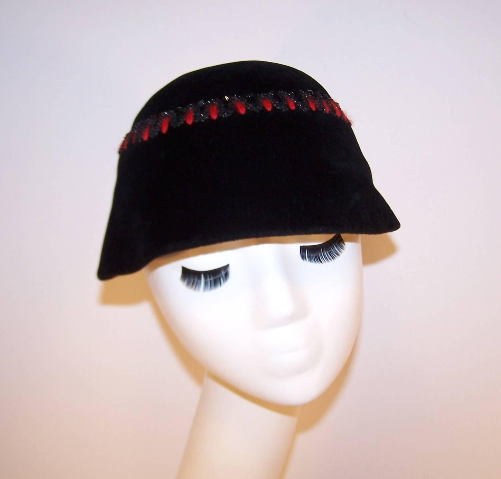 This C. 1950 Frances & Walter Nelkin hat sports the perfect contrast of a casual bucket style with glamorous vibrant red mohair embroidery and black beading.  The easy to wear body is a pliable black wool with a velveteen finish.  The crown is