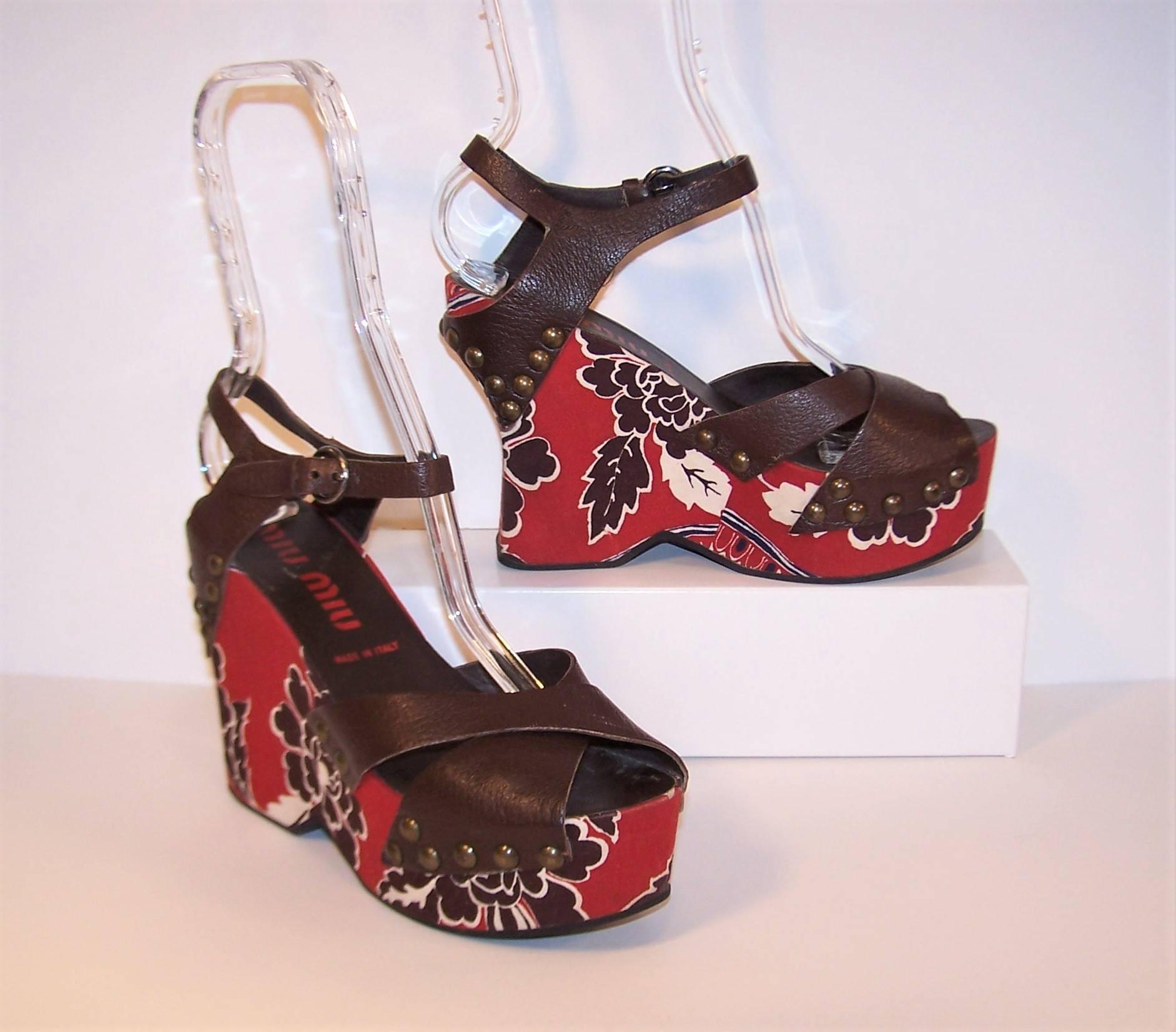 Exoticism prevails in these C.2000 platform wedge shoes from Miu Miu.  The dark brown leather upper crisscrosses for a peep toe effect at the front and securely buckles with an ankle strap at the back.  Brass nail heads attach the upper to the