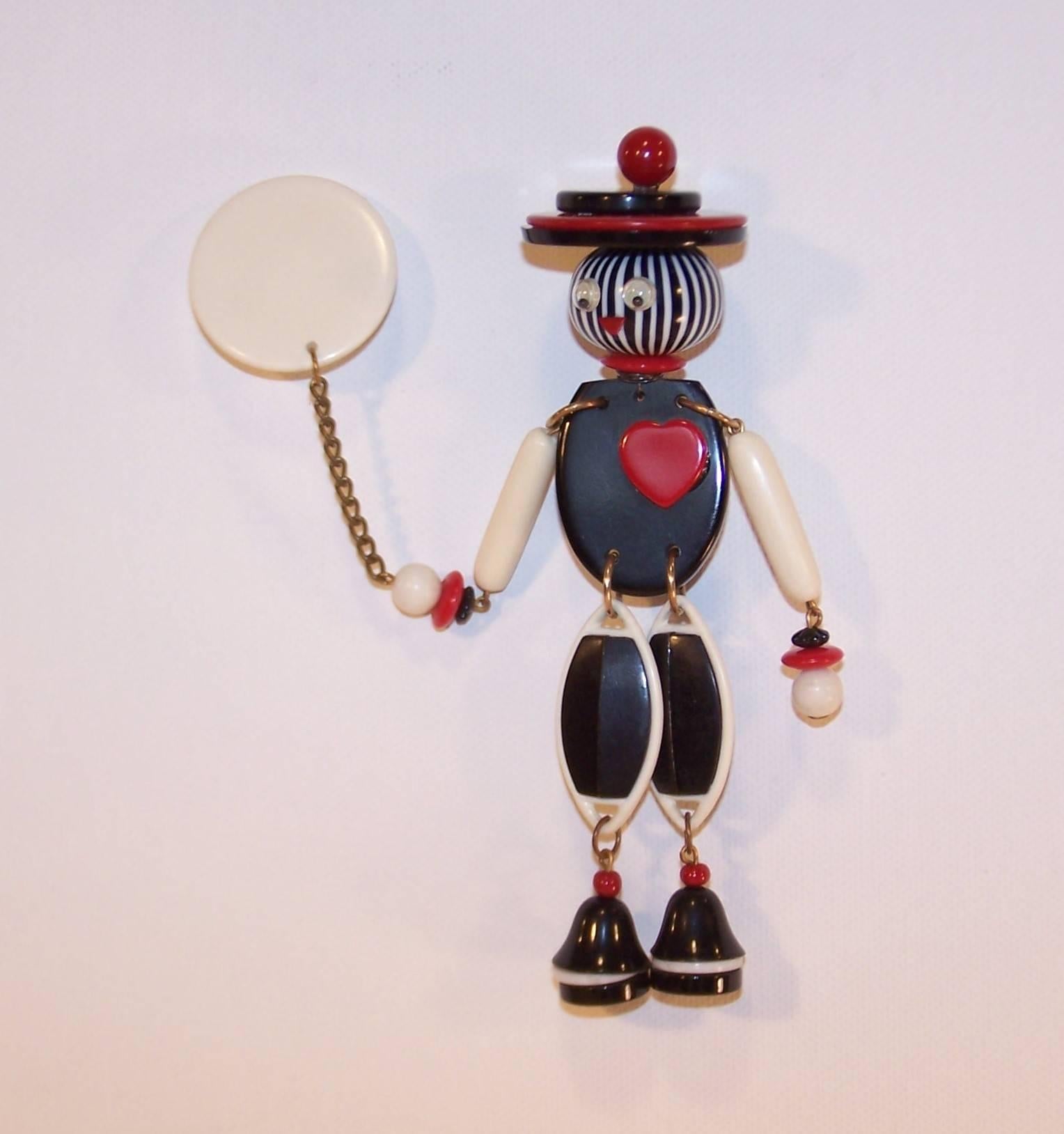 This little guy is loaded with fun loving personality!  The two part brooch consists of a disc balloon pin attached by a chain to an articulated man.  Both parts are designed with black, white and red bakelite with plastic segments secured by metal