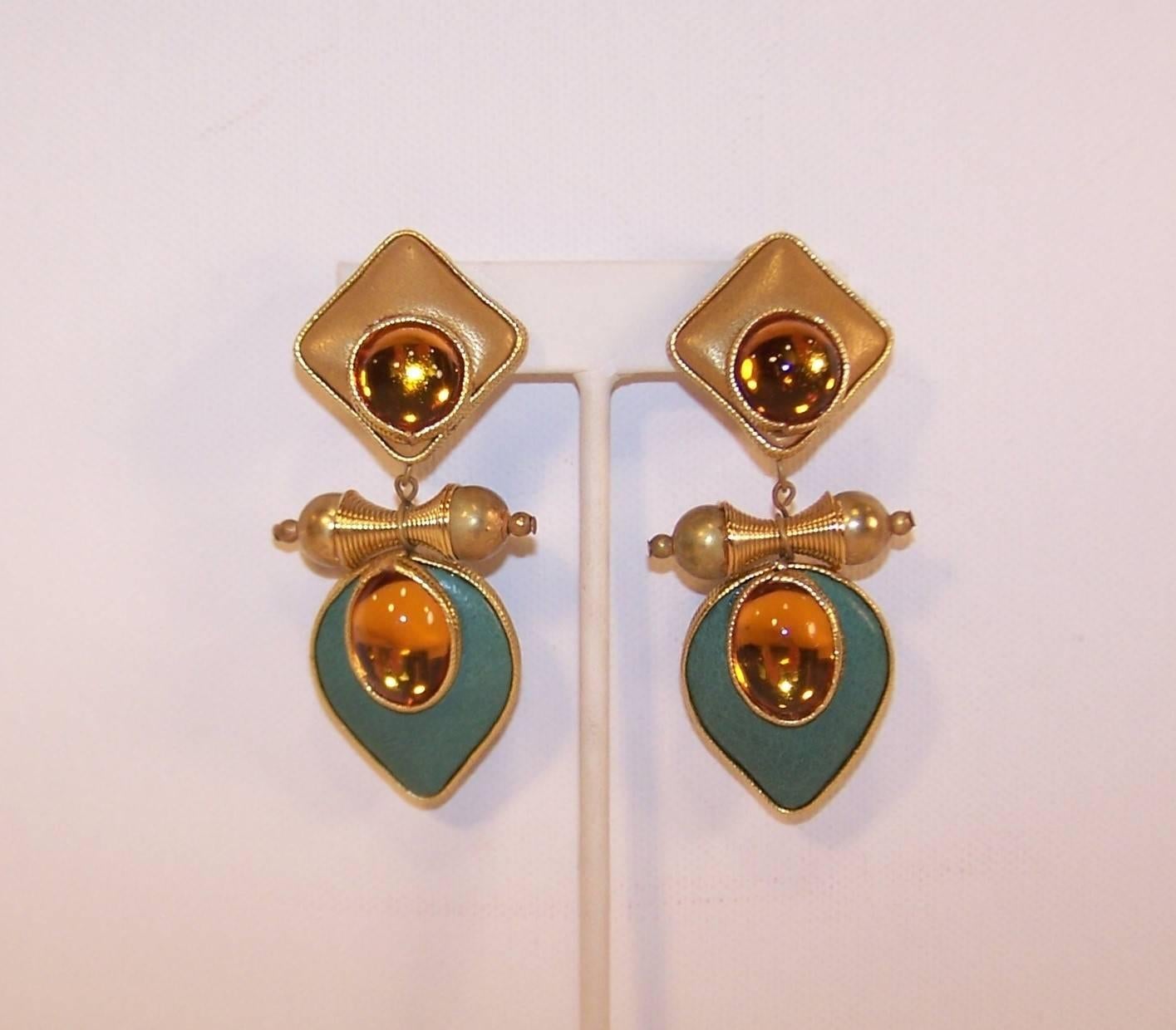 These 1980's drop dangle clip on earrings are a tactile and visual delight.  The base and drop dangle are covered in gold and light teal leather and framed in gold braid.  Each piece features a cabochon style faux amber stone also framed in braid. 