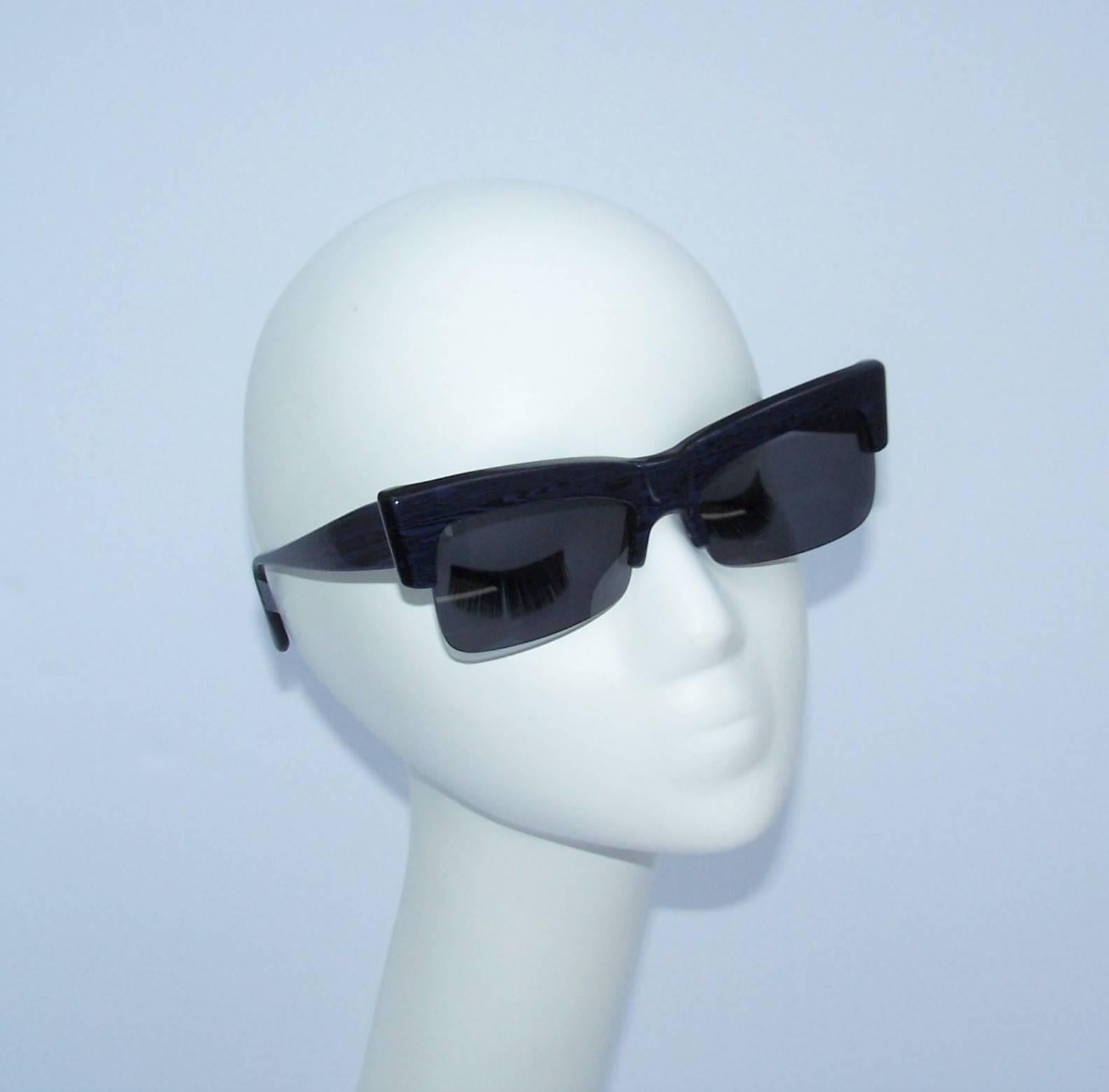 Don these futuristic Claude Montana sunglasses for instant cool factor.  The strong sculptural silhouette is created with a black and blue marbleized frame supporting open ended dark gray lenses.  Mr. Montana's revolutionary collaborations with