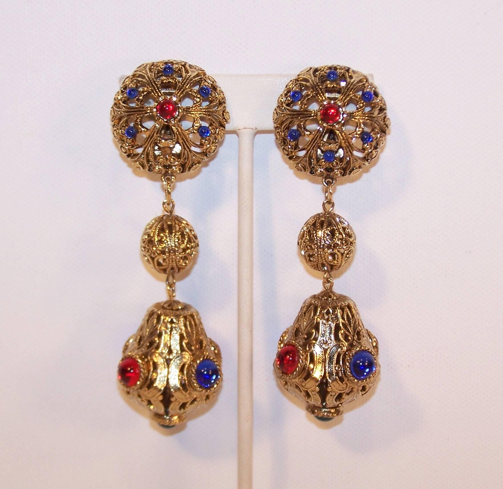These fabulously oversized dangle earrings by Gem-Craft are reminiscent of Moroccan lanterns.  The antiqued gold tone filigree metal orbs are decorated with cabochon decorations in red and royal blue with a surprise emerald green stone on the