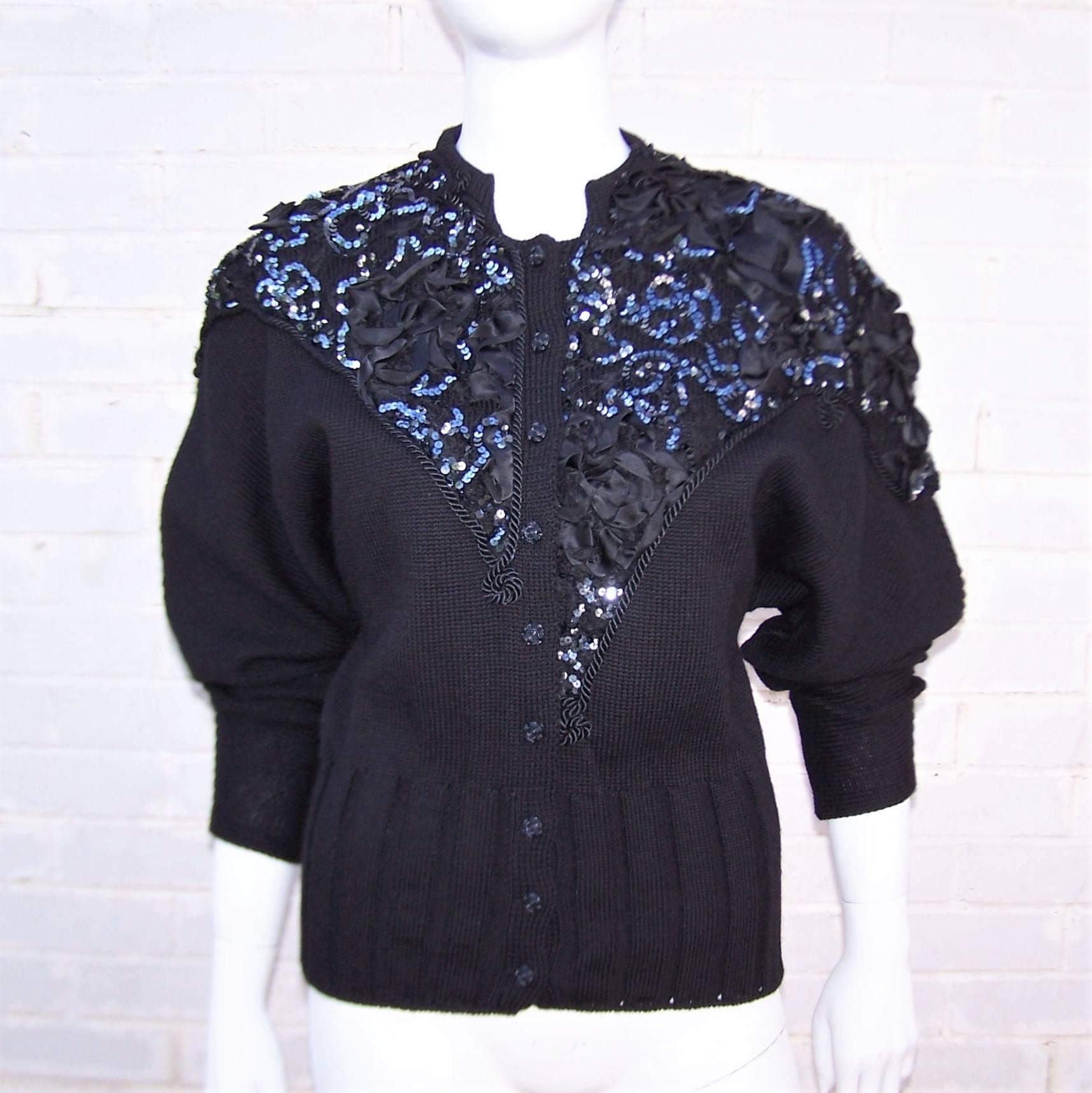 Bewitching and bedazzled!  Such is this 1980's French black wool evening sweater by Eva Picovski with an asymmetrical lace overlay adorned with satin ribbon rosettes, braiding and sequins.  It buttons up the front with an elongated ribbed waistband