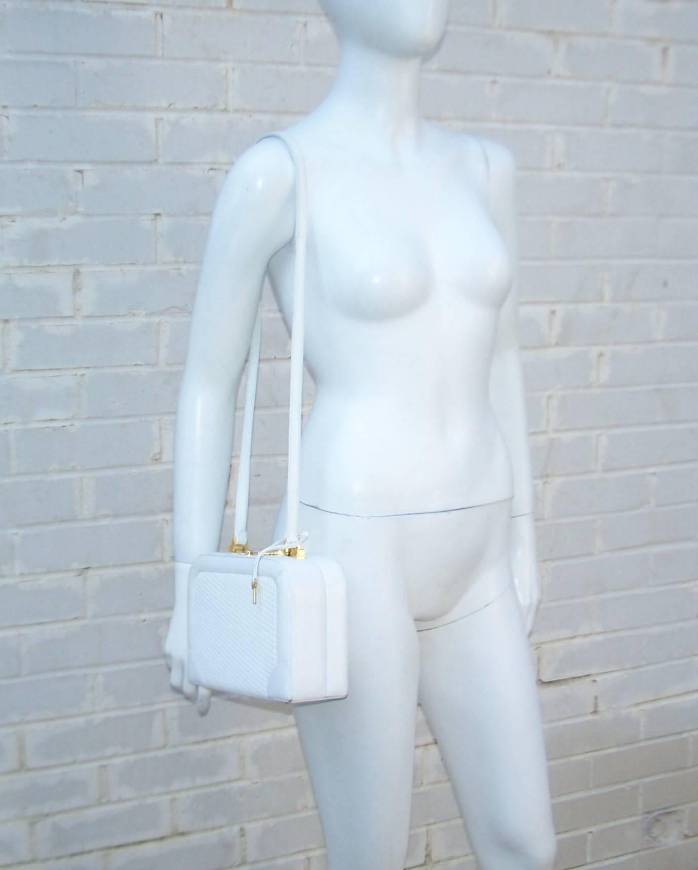 This clever Judith Leiber white calfskin leather handbag has the attributes of a train case with a gold tone push button locked closure accompanied by a mini key.  The versatile gold tone handle hardware slides open to allow conversion from a top