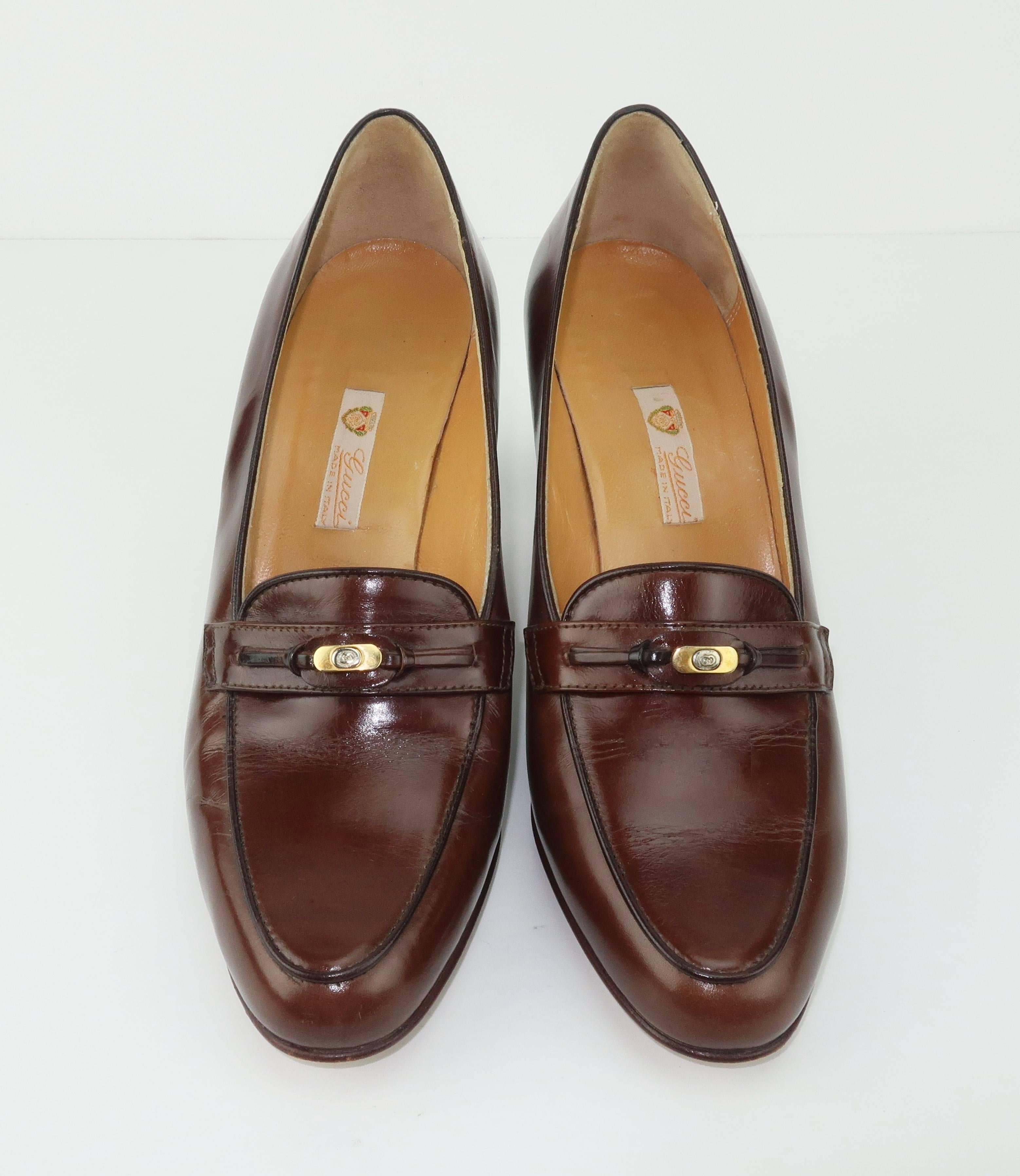 This preppy dark brown leather Gucci loafer is a classic paired with trousers, skirts or jeans. The vamp is decorated with a leather detail accented by a Gucci logo medallion in gold and silver metal.  The stacked wood heel is a comfortable