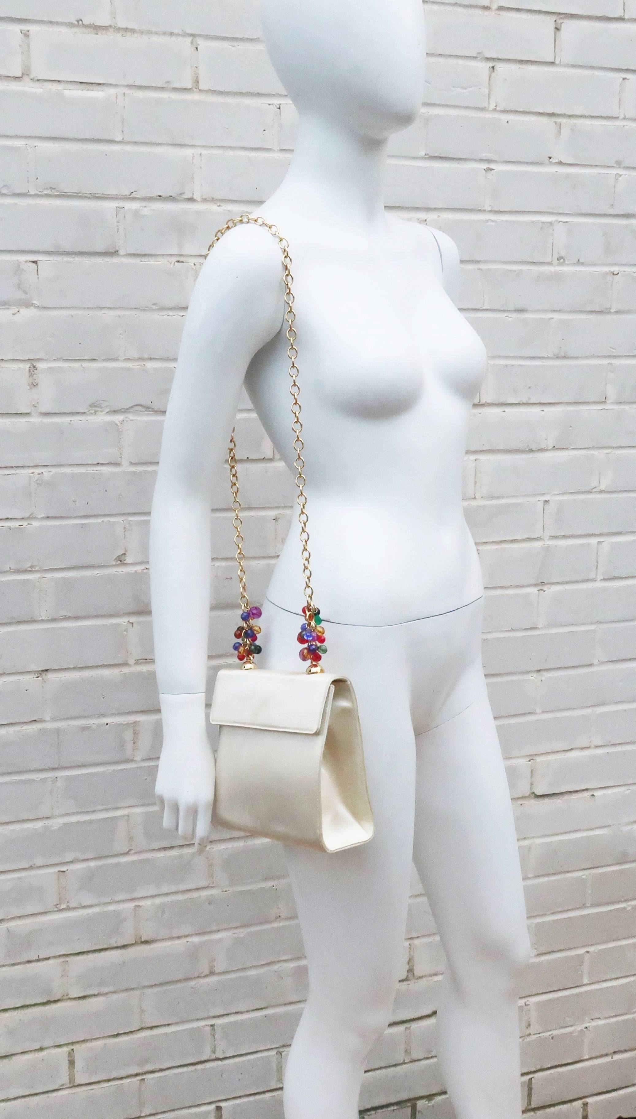 Charming ... in more ways than one!  This Italian creamy white satin handbag designed for Neiman Marcus has a gold chain shoulder handle decorated with faceted plastic charms in various shapes and colors.  The charms are akin to fruit on the vine