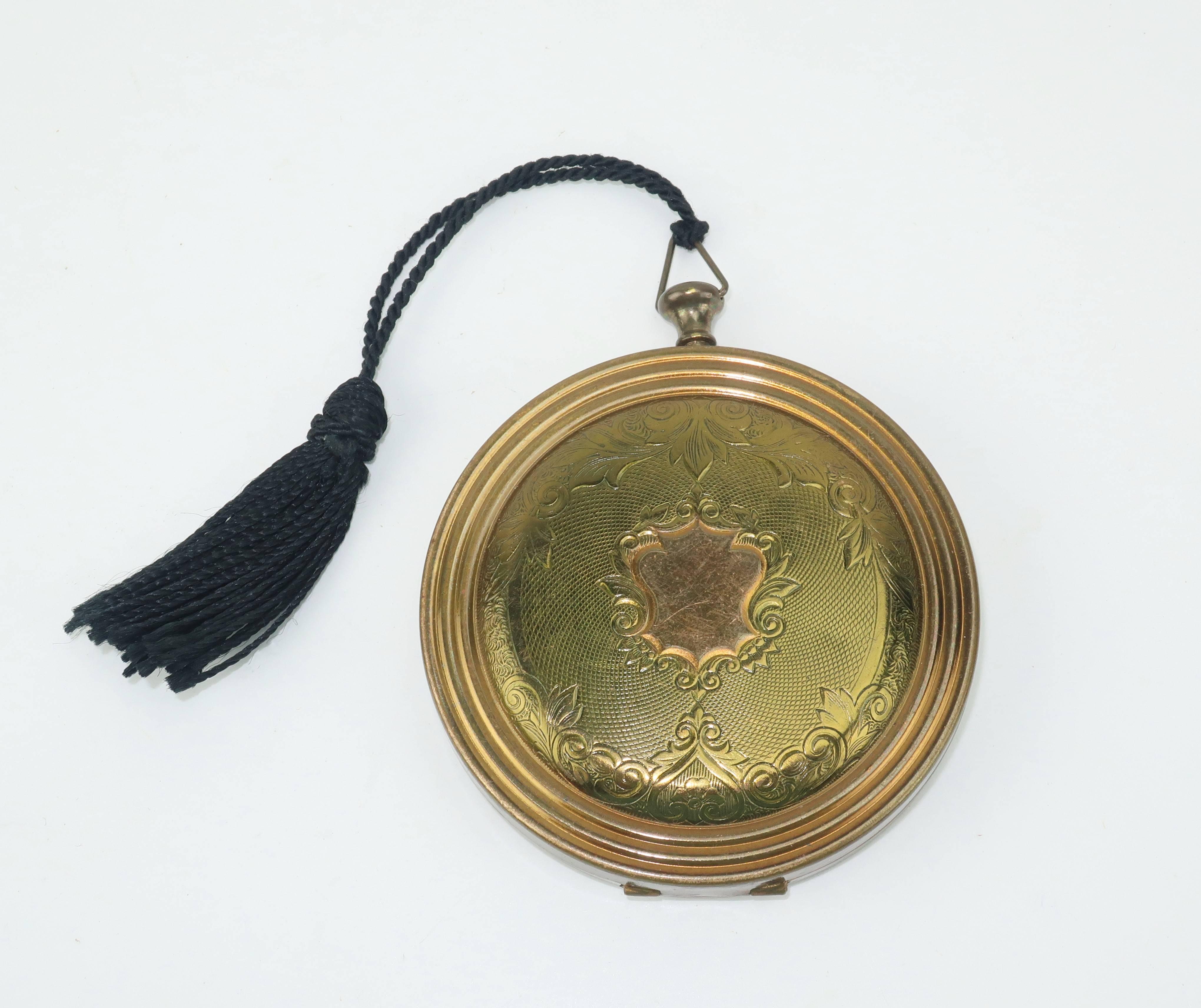 This unique Zell compact is designed to replicate a pocket watch complete with a push button ‘stem’.  The antique brass case has a Victorian era style machined decoration with a bullseye design on the back.  The interior displays a mirror, loose