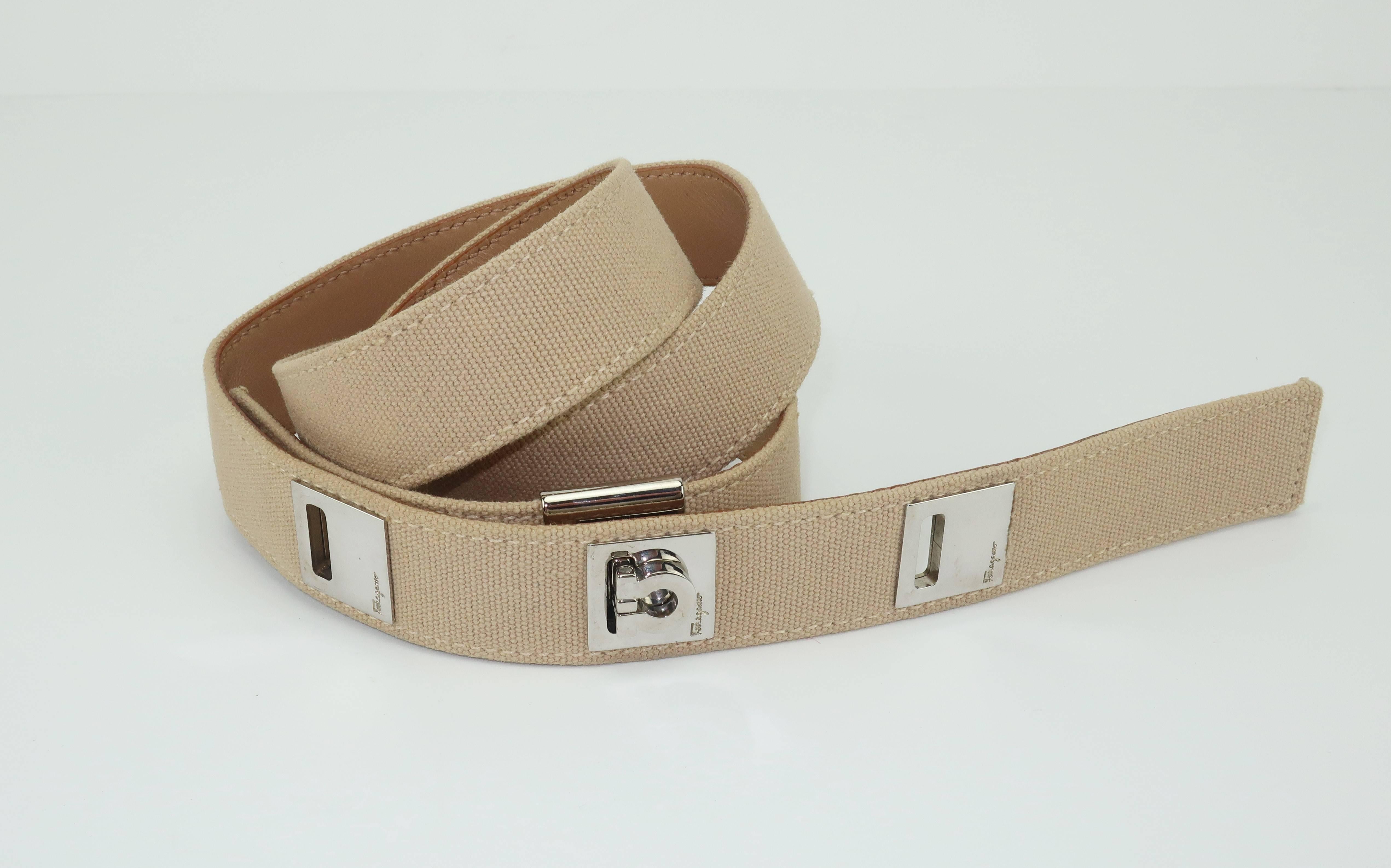 This belt by Ferragamo has the elements of a fashionable safari style with a unique contemporary chromed silver logo buckle.  The light beige canvas body is backed by a coordinating leather and accented with three slotted chrome squares impressed