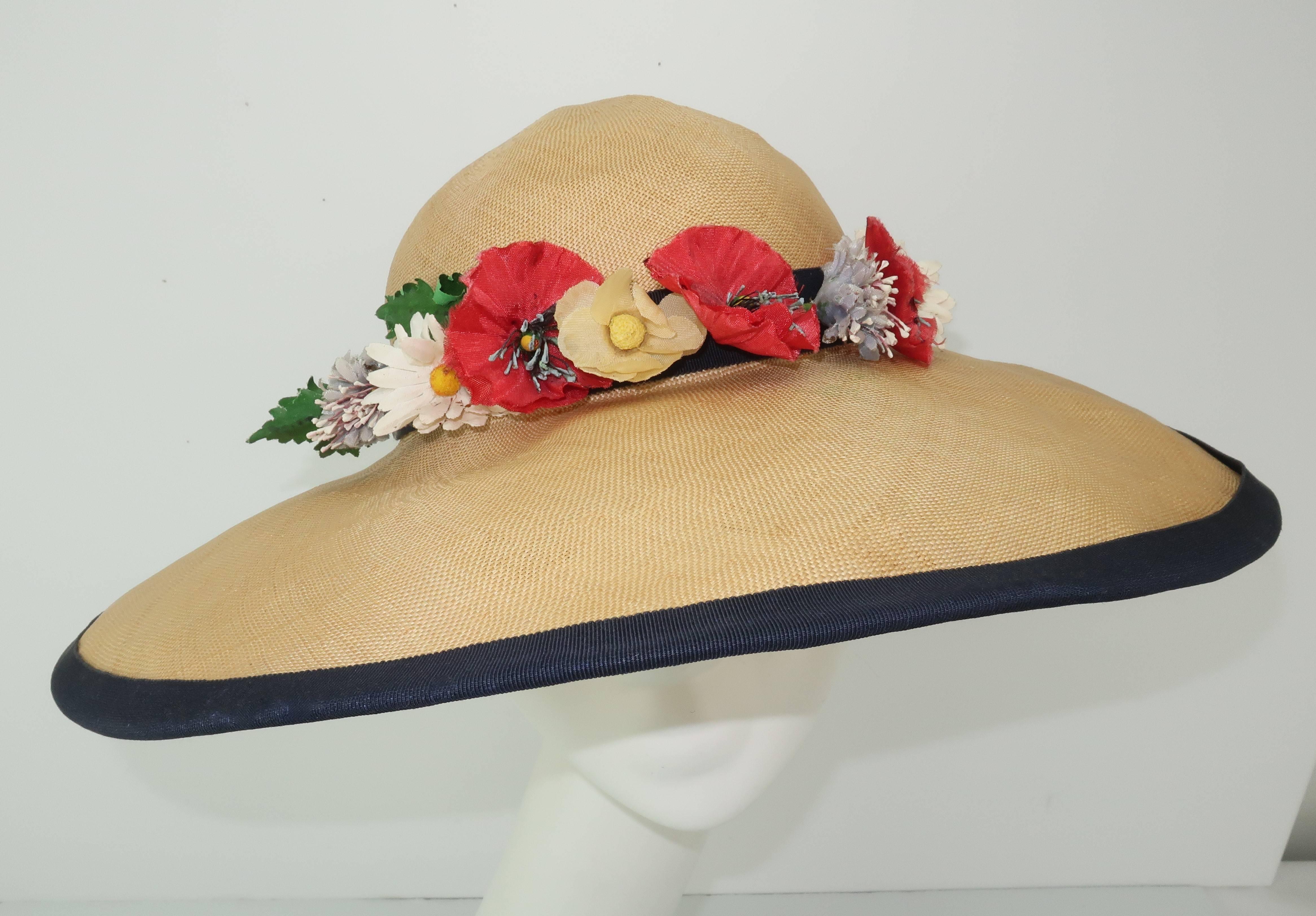 Garden party anyone?  This C.1950 wide brimmed natural straw hat by Christine Original is edged in navy blue grosgrain ribbon and decorated with a bouquet of colorful silk flowers including shades of poppy red and daisy white mixed with pale blue,