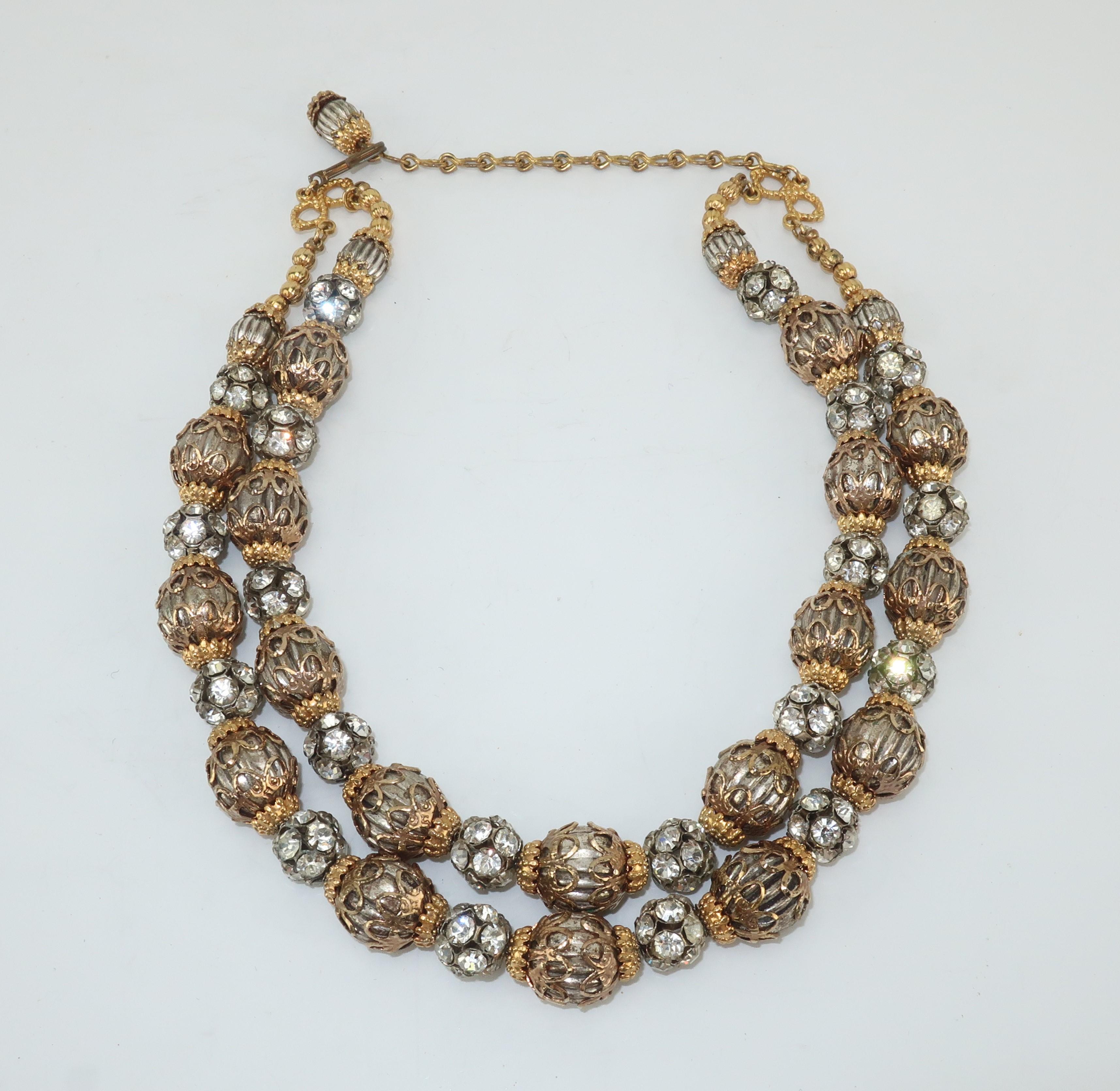 A 1950’s dazzler!  This two stranded necklace consists of silver tone fluted beads with gold tone filigree caps interspersed with rhinestone encrusted beads.  It is outfitted with adjustable hook and chain enabling wear as a choker or short necklace