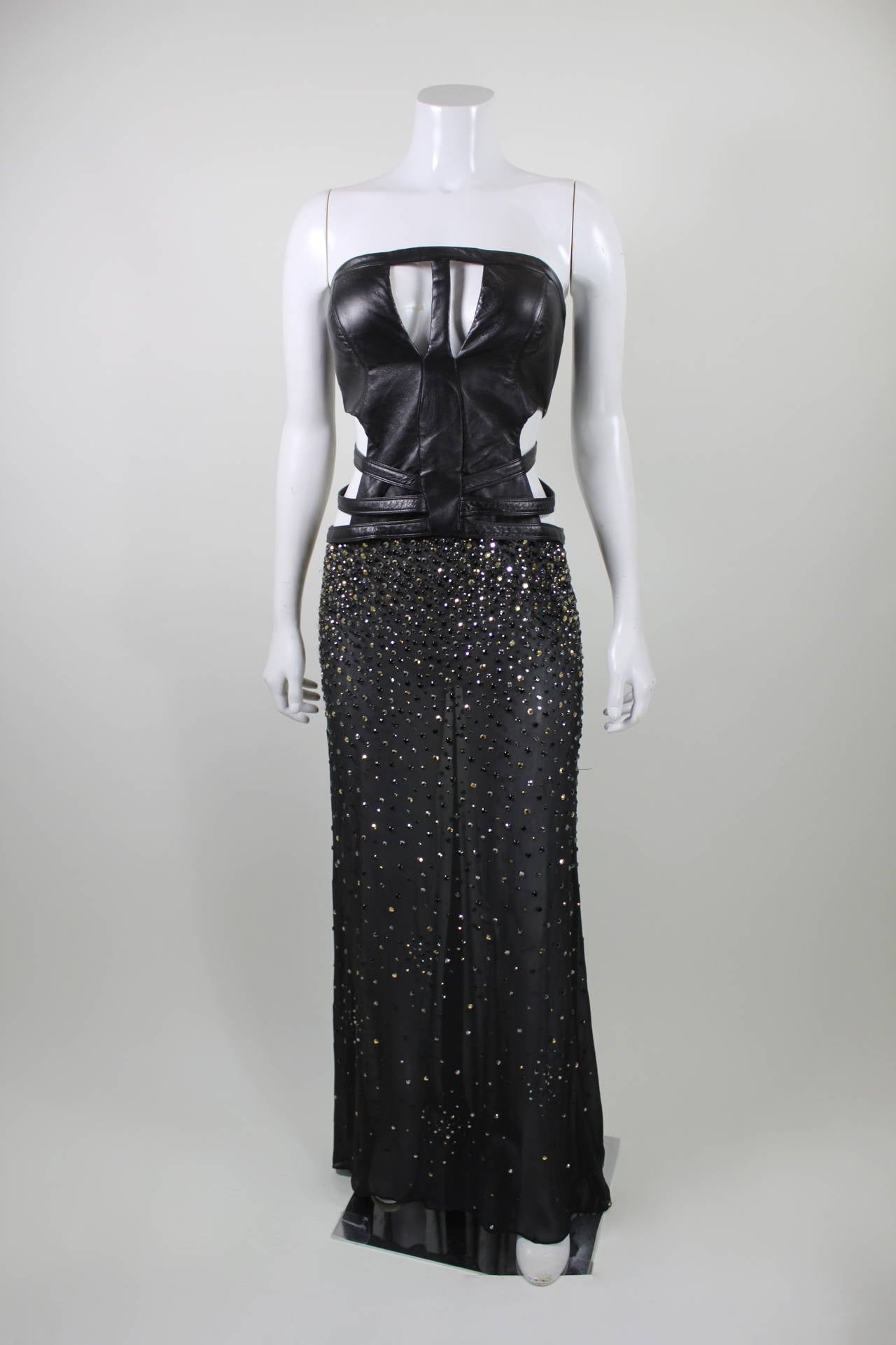 A jaw-dropping, ultra sexy gown from Versace. The bodice is done in supple, luxurious leather. Adjustable straps at the waist ensure a perfect, body-hugging fit. A sheer black chiffon skirt is embellished with prong-set rhinestones, in dazzling
