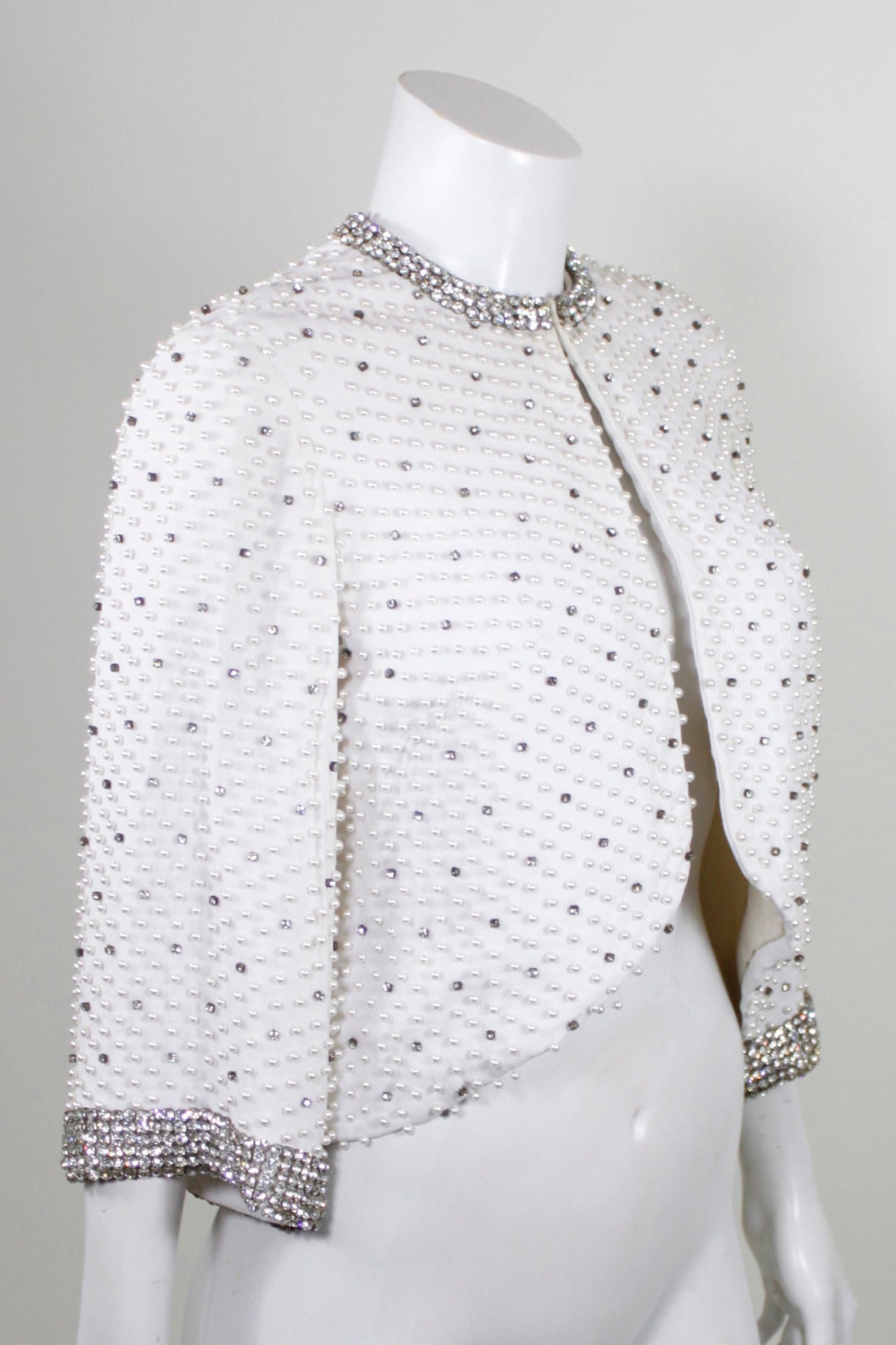 A gorgeous evening jacket from the 1960s. Beautiful cream rayon crepe is embellished with pearls and beads throughout. The collar and cuffs feature dazzling rhinestone trim. The silhouette is a-line with bell sleeves. 

Measurements--
Bust: up to