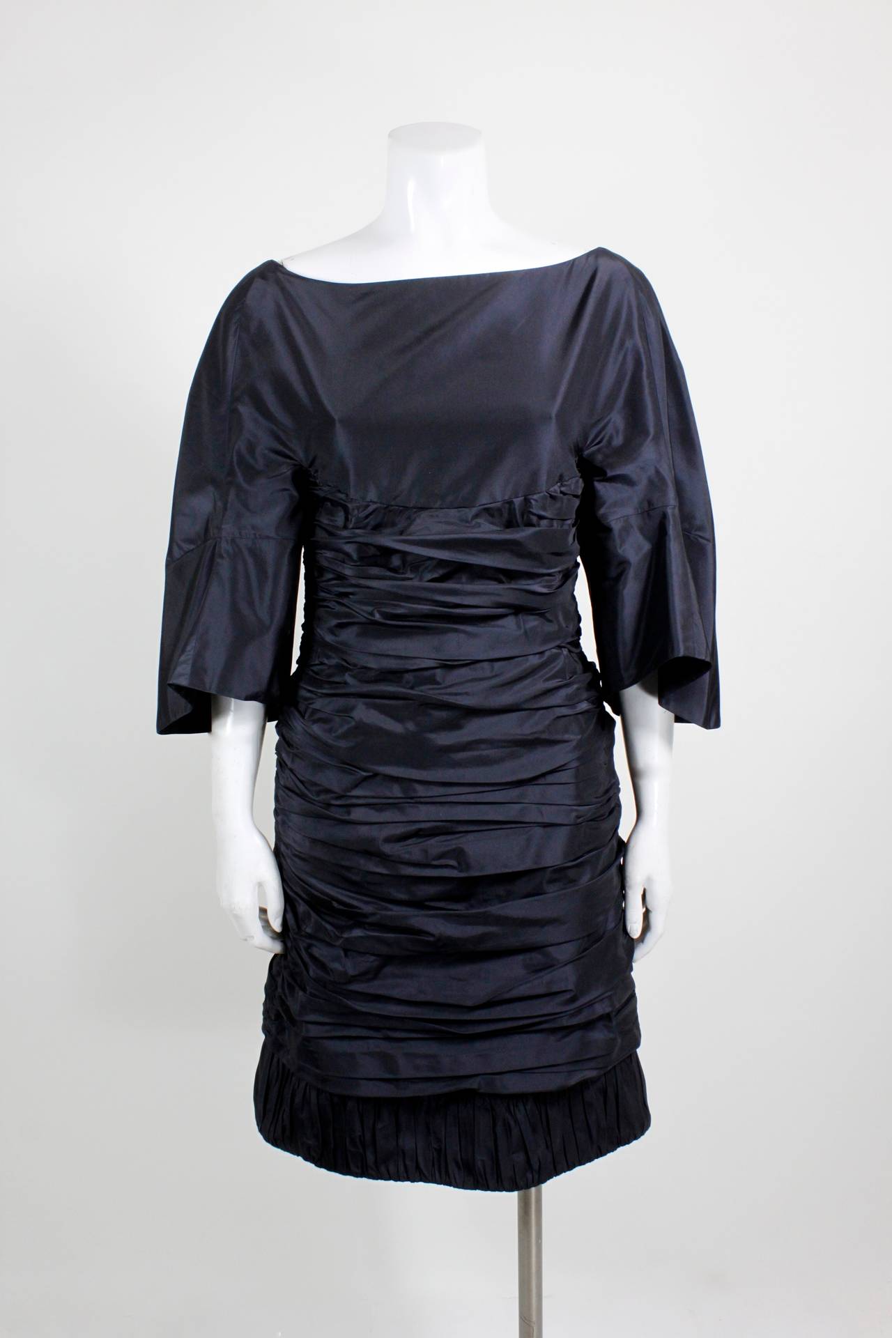 A stunning black taffeta cocktail dress from Ralph Rucci. An architectural bodice is streamlined with a carefully ruched skirt. The back of the gown features a dipped v-back with a tie-back swag: the perfect balance of modernism and femininity.