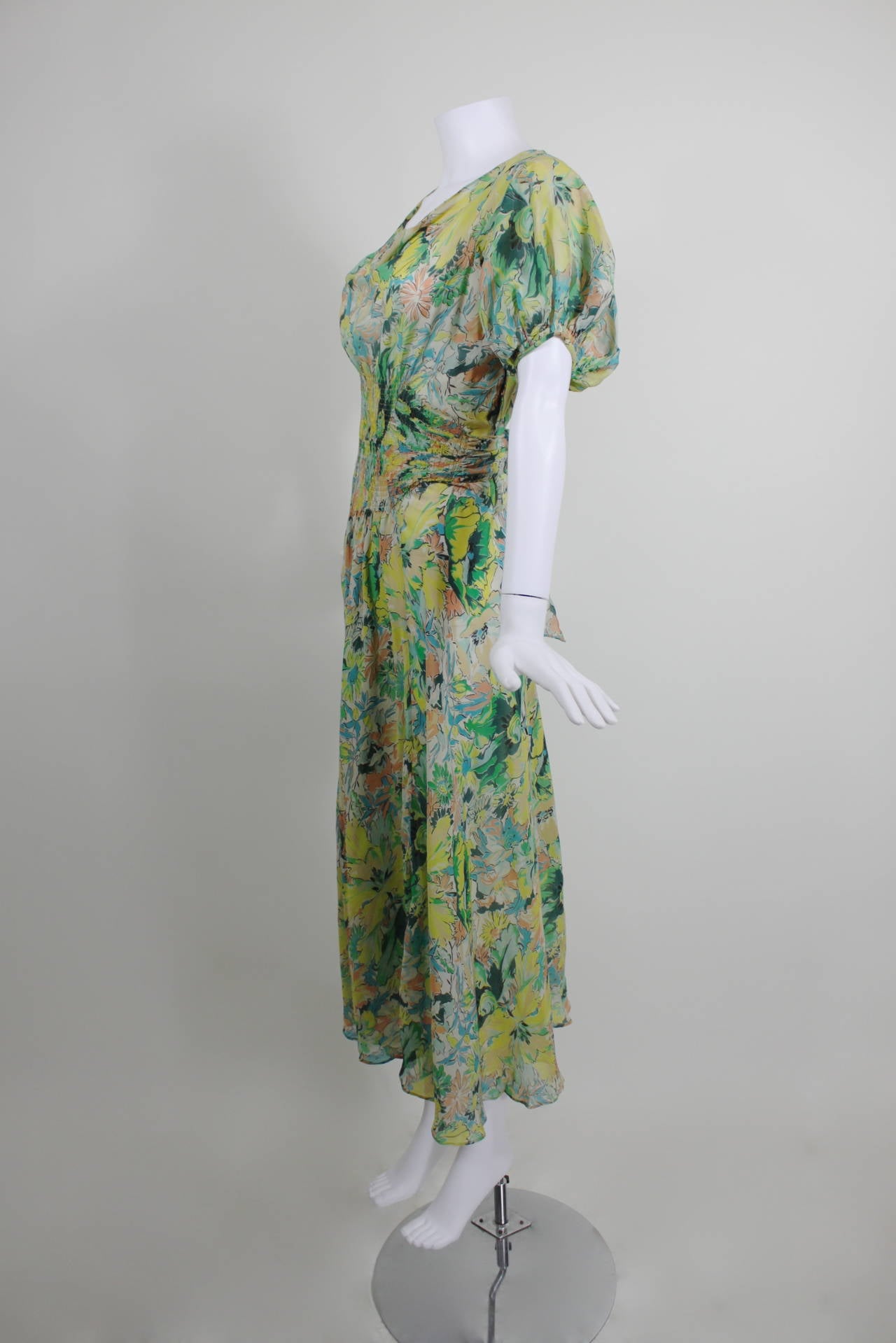 This dress is a gorgeous example of 1930s floral chiffon. Featuring a vibrant, colorful, painterly floral print, the dress has princess sleeves, a blouson bodice, and beautiful smocking at the waist. The tea-length skirt is lovely and