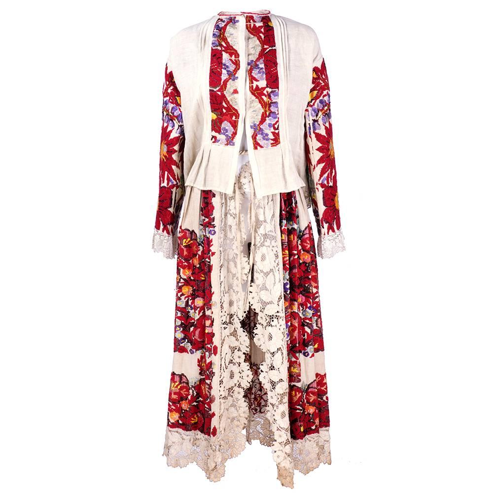 Two piece Serbian/Croatian ensemble consisting of rough cotton blouse with extensive embroidery in abstract floral pattern and trimmed in crochet lace. Snap closure in front. Flare pleats in rear. Also included is open apron style full length skirt.