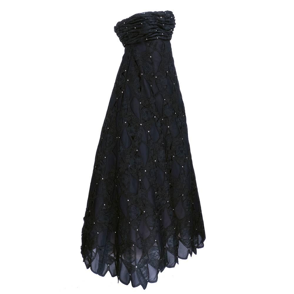 Dramatic strapless gown by Scaasi. In black lace with inset rhinestones. Fully lined, empire waisted. Tulle petticoat make skirt very full. Boned bodice makes very structured silhouette. Shirred top. Scalloped hem.