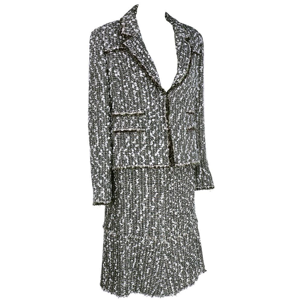 Late Chanel suit in black and white in  a nubby rayon wool blend. Classic boxy cut jacket with frayed hem - open front. Tulip hemmed skirt. Silver-tone logo buttons at cuff. Classic grey embossed camelia print lining.

Skirt-
Waist: 30"
Length: