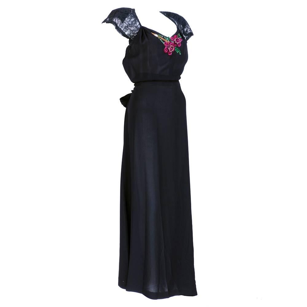 Classic 1940s look. Lightweight black rayon crepe with self tie belt and lace peek a boo back. 3-D sequin floral applique.  Simple yet elegant. 