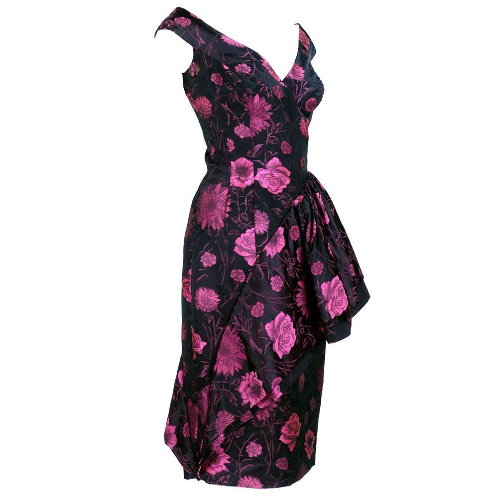 Super sexy 50s cocktail dress in black and pink floral jacquard with amazing swirling swag from hip to hem. Perfect wiggle dress! Unlined,zip up side and beautifully finished.