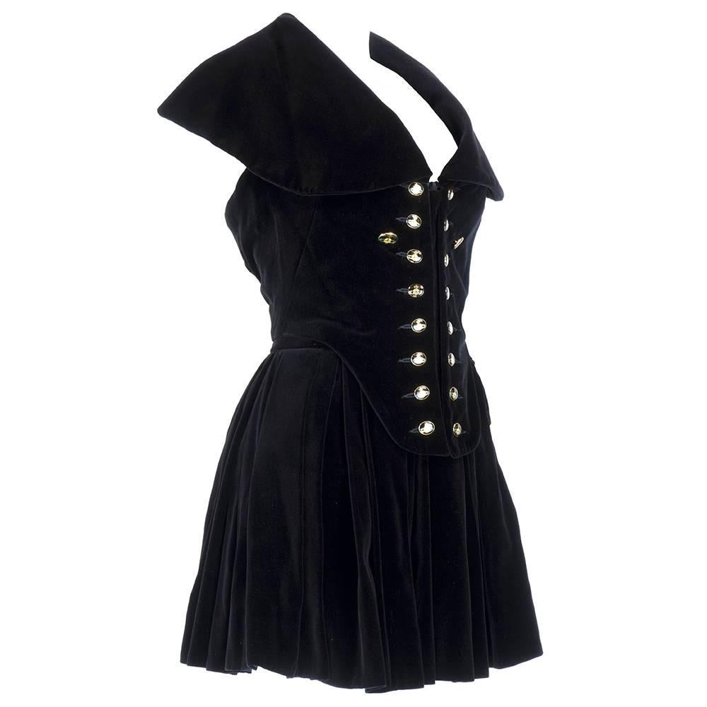 Vivienne Westwood black velvet ensemble circa 1990s. Consisting of dramatic bustier - fully boned - with halter and oversized collar. Zips and buttons up front with enamel logo buttons. Paired with full, pleated mini skirt. Super