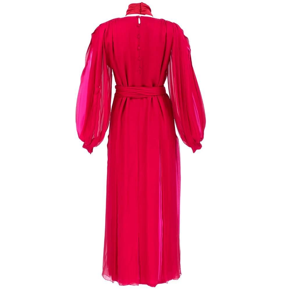 Dramatic and extravagant gown circa 1980s by James Galanos. Red Chiffon -pleated at hips with pink accents underlaid. Full, pleated sleeves that button at cuffs. Includes half slip, long sash belt and wide detached choker with oversized bow. Buttons