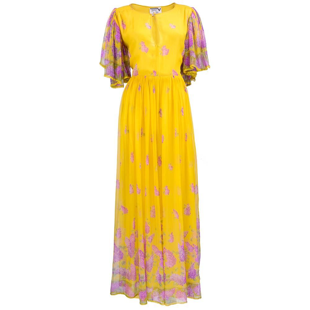 Floaty and feminine maxi dress in yellow 100% silk chiffon by Valentino circa 1970s. With purple floral print scattered about. Fan sleeves with gathered full skirt. Fully lined. With matching long scarf. Small repair near hem and several small spots