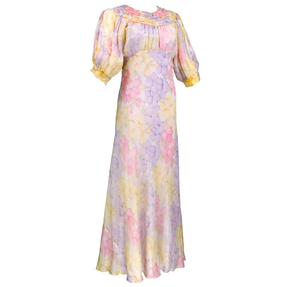 One of the prettiest 1930s bias cut lawn dresses we have ever had. Floral print in pastel hues. Smocked yoke and full half sleeves. Snaps at side with covered buttons at neck. Comes with pale mauve slip that has some discoloration that is not