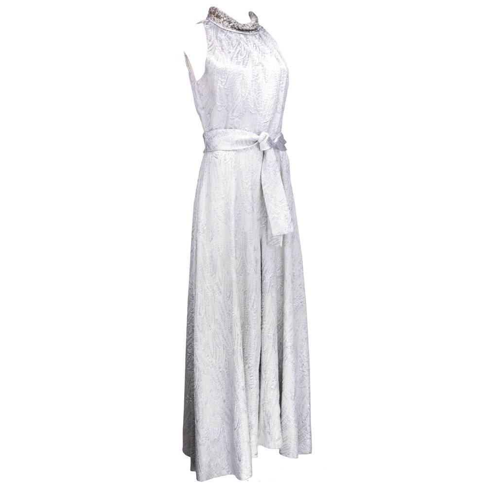 Swinging 60s silver metallic jumpsuit with sequin embellished  collar. Groovy swirling abstract pattern. Wide lag palazzo pant bottom with high beaded neckline. Comes with matching sash tie. Zips up back.