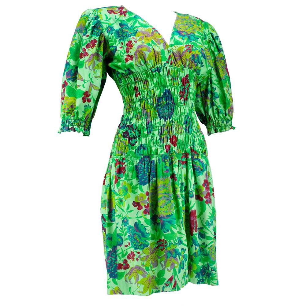 Vibrant tropical florals adorn this lightweight cotton confection by Ungaro circa late 1970s. Cheerful green with wide smocked waist and cuff. Gathered skirt that ends above the knee. Slightly padded shoulders. Sizing slightly flexible because if