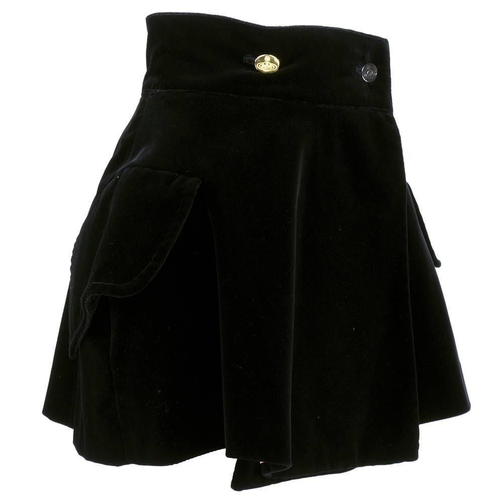 Gold label Vivienne Westwood mini skirt in black velvet. Flared, wrap style with hip pockets that create a pannier vibe. Fully lined in nude satin with trademark log buttons. Beautifully tailored.