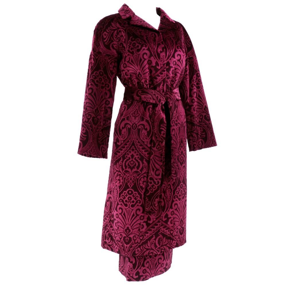 Au courant  styling. Circa 1990s ensemble by Dolce and Gabbana in shaved burgundy velvet with paisley pattern. Outfit consists of lightweight, button front coat that snaps up front and has matching sash belt - matched with mid-calf pencil skirt.