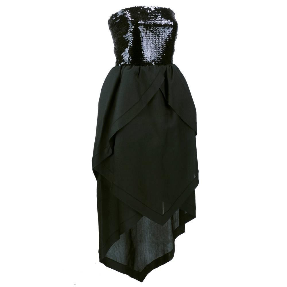 Dramatic  gown by Pierre Cardin circa 1980s. Black sequin strapless top with tiered mid length skirt. Zip up back, half lined. Skirt is layered - tiered from short to long in back. Architecturally stunning yet still sexy.  Shiny, large scale sequins