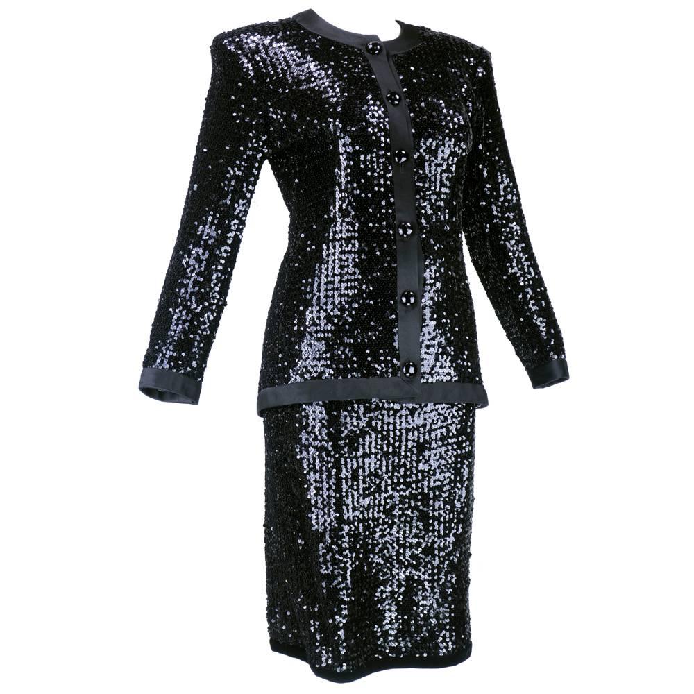 Classic and timeless piece by Yves Saint Laurent circa 1980s. 2 piece ensemble with black sequins. Collarless jacket trimmed in black satin with faceted black glass buttons. Jacket and skirt fully lined. Sharp padded shoulders - attached sash. Skirt