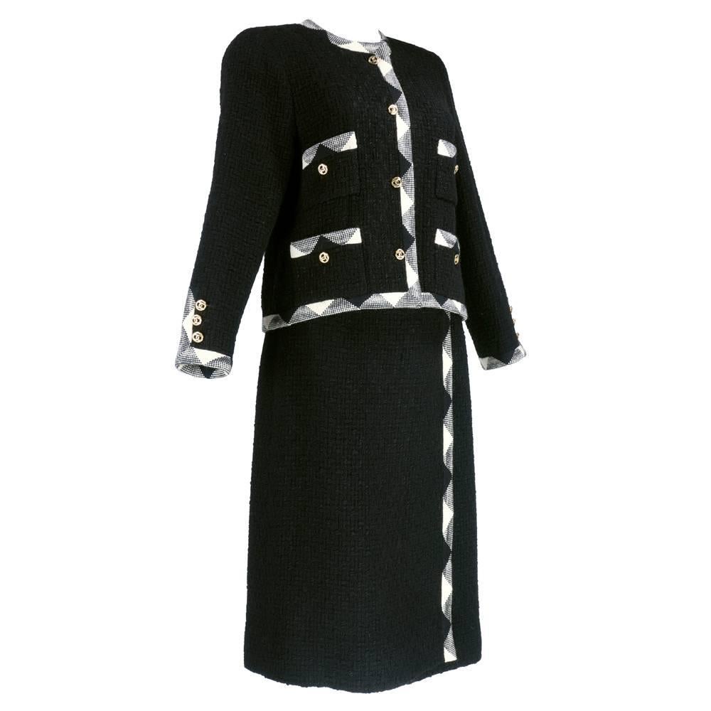 The most iconic piece in fashion history - the little black suit by Chanel circa 1960s.   Boxy cut jacket in nubby  100% wool. Trimmed in contrasting black and white woven fabric. Double C log buttons. Slightly flared wrap style skirt. Beautifully
