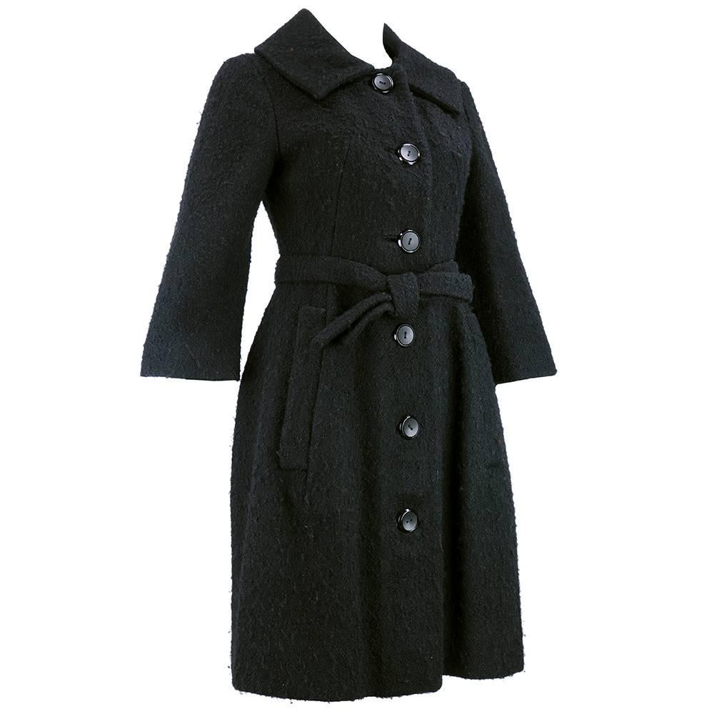 Exquisitely tailored coat by French couturier Jacques Heim circa late 1950s - early 1960s. Black nubby wool with fitted bodice and flared bottom. Sash tie belt. Fully lined with oversized buttons and exaggerated foldover collar.