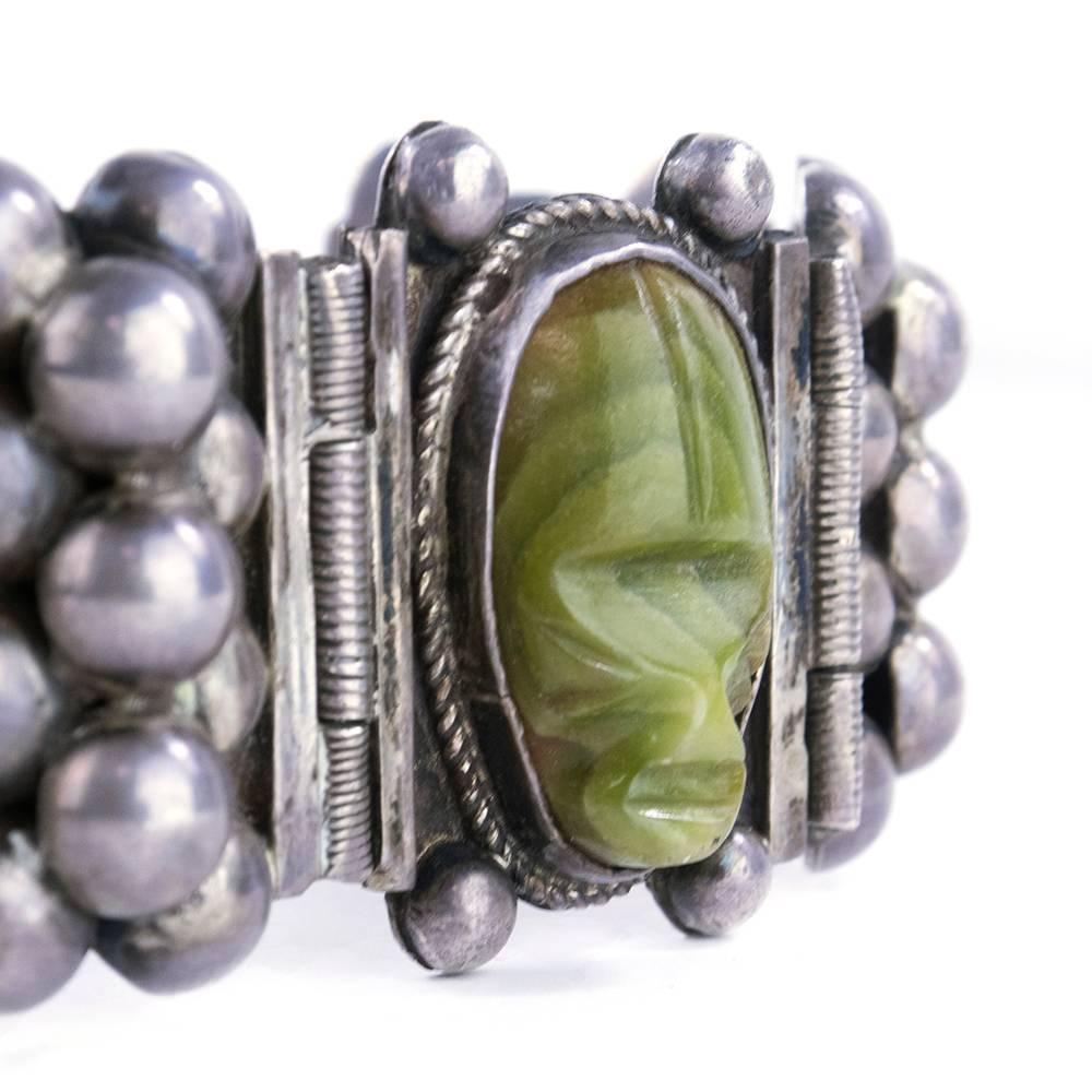 This outstanding Mexican silver bracelet is made from alternating links of granulated metal and bezel set cabachons. The granulated links have three rows of silver half domes. The cabachons have a mask motif cut from polished olive green agate. The