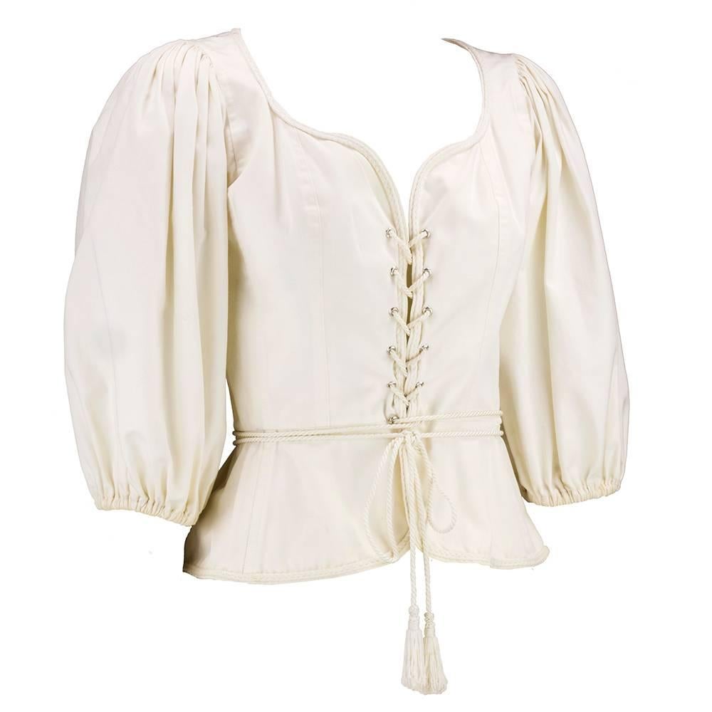 A timeless classic. An Yves Saint Laurent peasant style blouse in the lace up style circa 1970s. ivory cotton with sexy neckline, lace up bodice and three quarter sleeves gathered at cuff. Fitted at waist with short peplum. One of YSLs most iconic