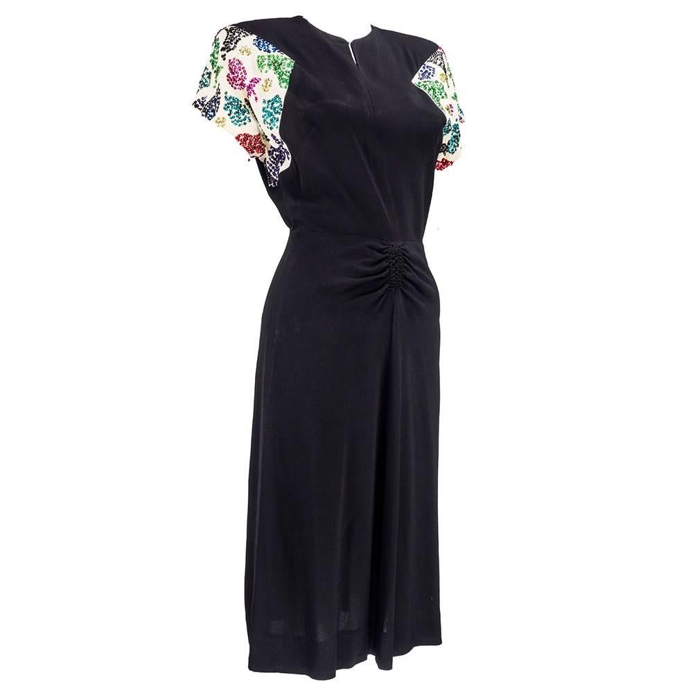 Vibrant and noir at the same time. A circa 1940s black crepe dress with white cap sleeves and padded shoulders. Ruched at waistline with slightly flared skirt.