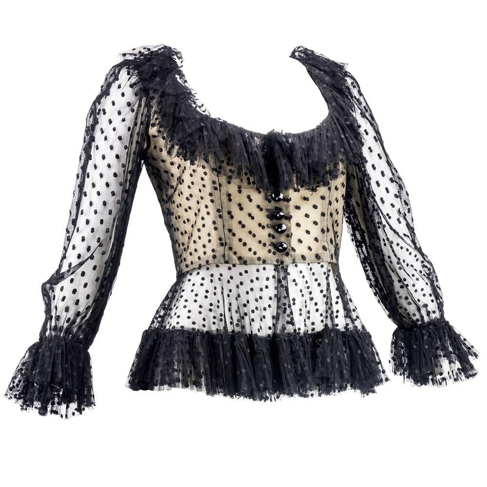 Flouncy and flirty evening blouse by Oscar de la Renta circa 1980s. Black polka dotted net with ruffled deep cut neckline, hem and cuff. Backed in nude. Closes with black faceted jet buttons down front.