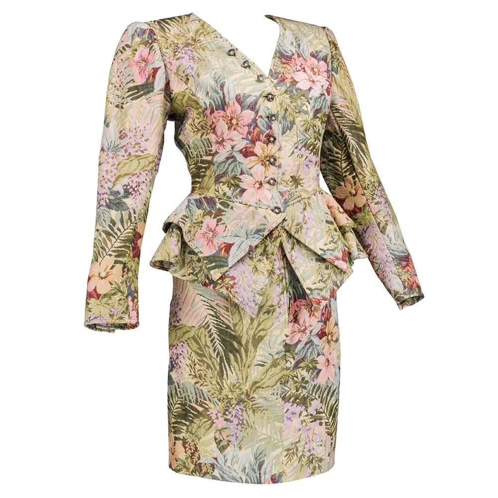 Circa 1980s Emanuel Ungaro ensemble of fitted jacket with layered jutting peplum and matching fitted short skirt. In delicate painterly floral in muted pastel tones.  In cotton/rayon blend with rayon lining. Delicate silver-tone buttons in half clam