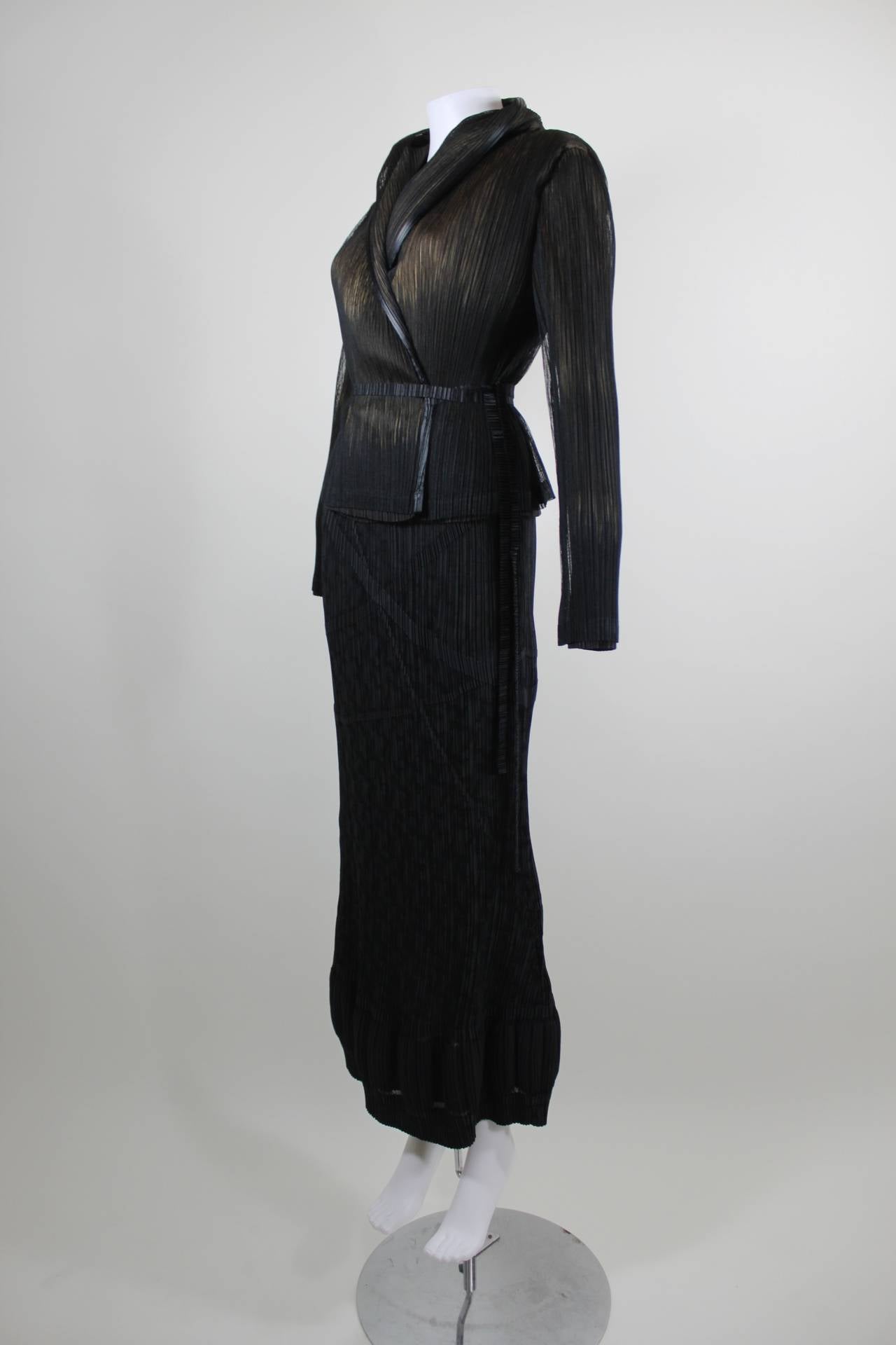 A fabulous ensemble from Issey Miyake. The jacket features a removeable shawl collar; the sheer black pleated fabric rests on a nude base, adding depth and texture. Jacket wraps with a thin pleated belt. The column skirt features a banding pattern