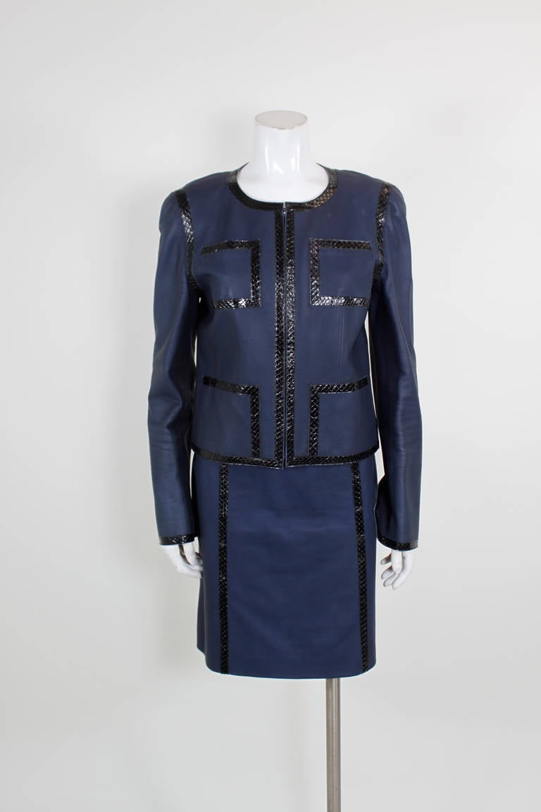 A luxe leather ensemble from CHANEL. Done in a rich navy leather and trimmed with black snakeskin around the collar, pockets, and waist of the skirt. Fully lined in iconic CHANEL camellia print silk.

-Jacket zips in front. Skirt zips in