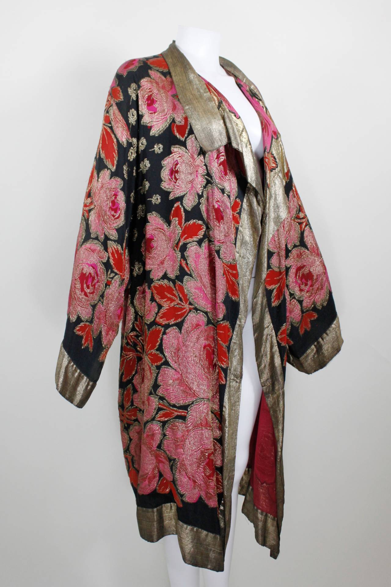 A gorgeous day or evening coat from the late 1920s, featuring a vibrant red and pink rose print with gold lamé throughout. Trimmed in a shimmering strip of gold lamé, and features a 