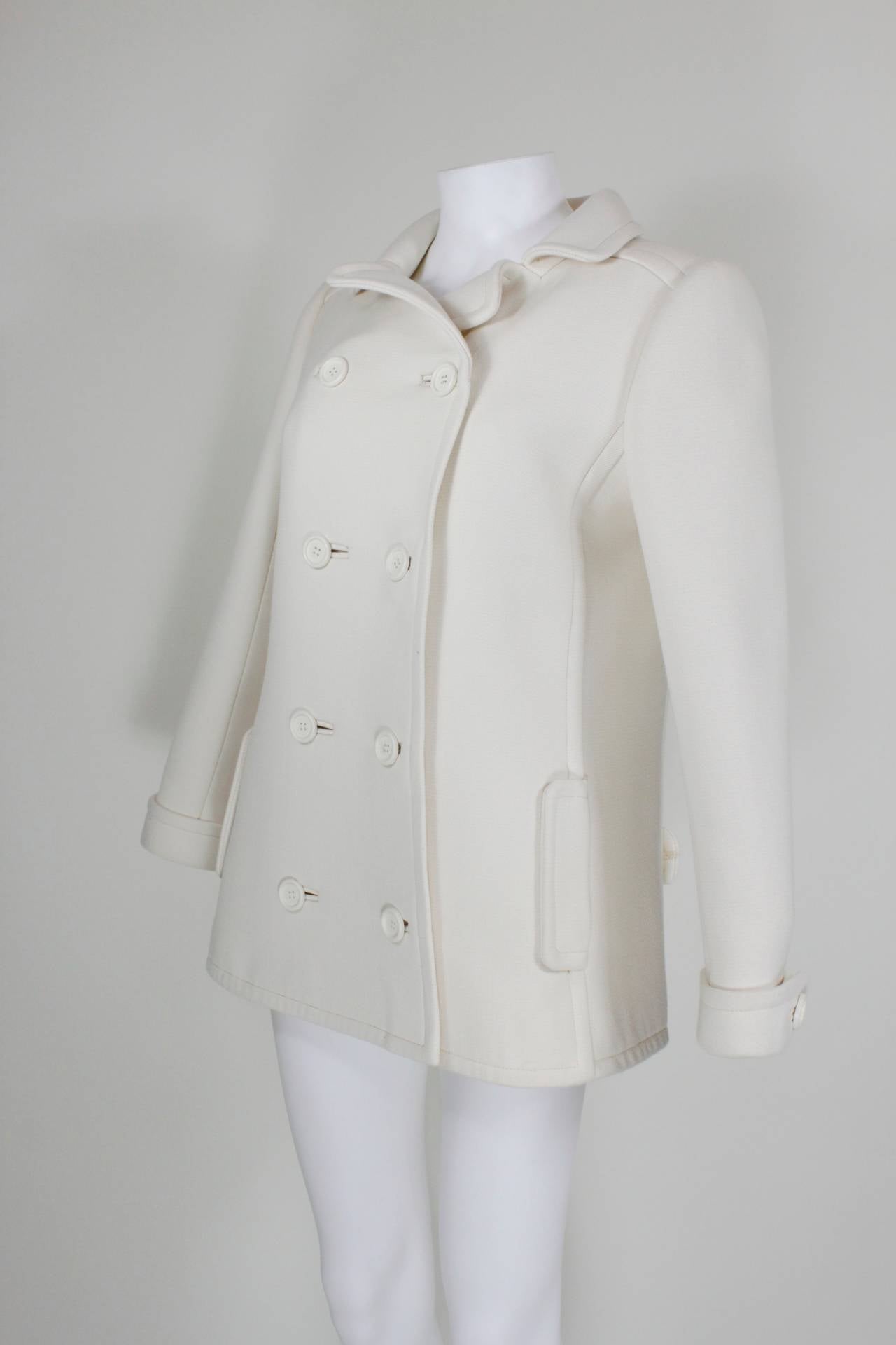A creme wool peacoat from Courréges, featuring a double-breasted, waist-length silhouette with a collar, cuffed hems, and band across the back. Fully lined. 

Measurements--
Bust: up to 40 inches
Waist: up to 38 inches
Hip: up to 42