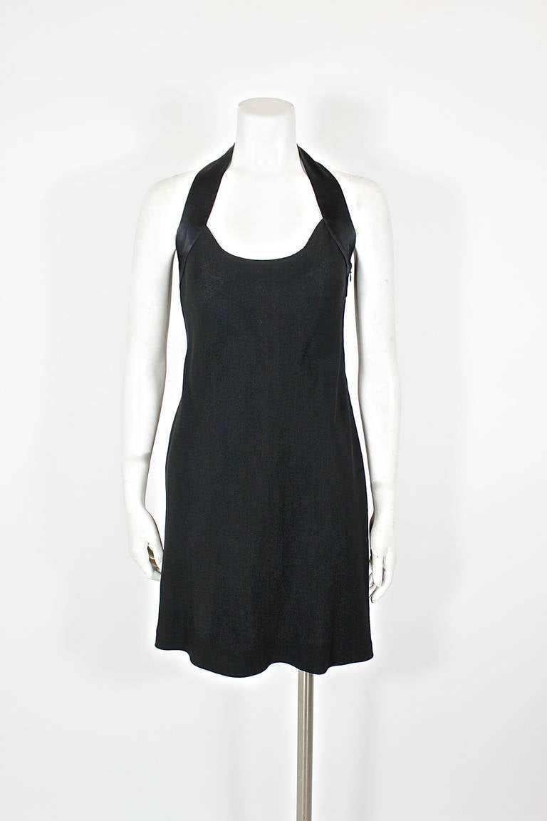 A black crepe dress from Moschino Cheap & Chic, accented with black satin straps that form a peace sign in the back. Dress features a flowing skirt and pockets.
-Marked a US Size 8
 
Measurements--
Bust: 34”
Waist: up to 28”
Hip: free
Length,