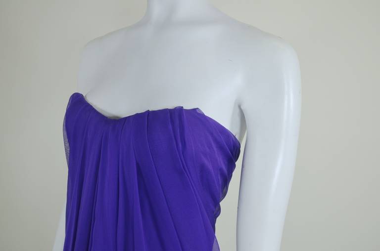 An ethereal strapless gown from iconic fashion designer Alexander McQueen. Done in layers of rich royal purple, the gown is bold and feminine. The chiffon appears to flow from the bodice and back of the gown, pooling in a beautiful goddess