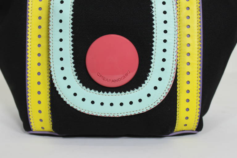 A chic and playful canvas handbag from Moschino. Accented with light pink, yellow, purple, and blue leather detail. Handbag features a zip closure with bauble charm.
