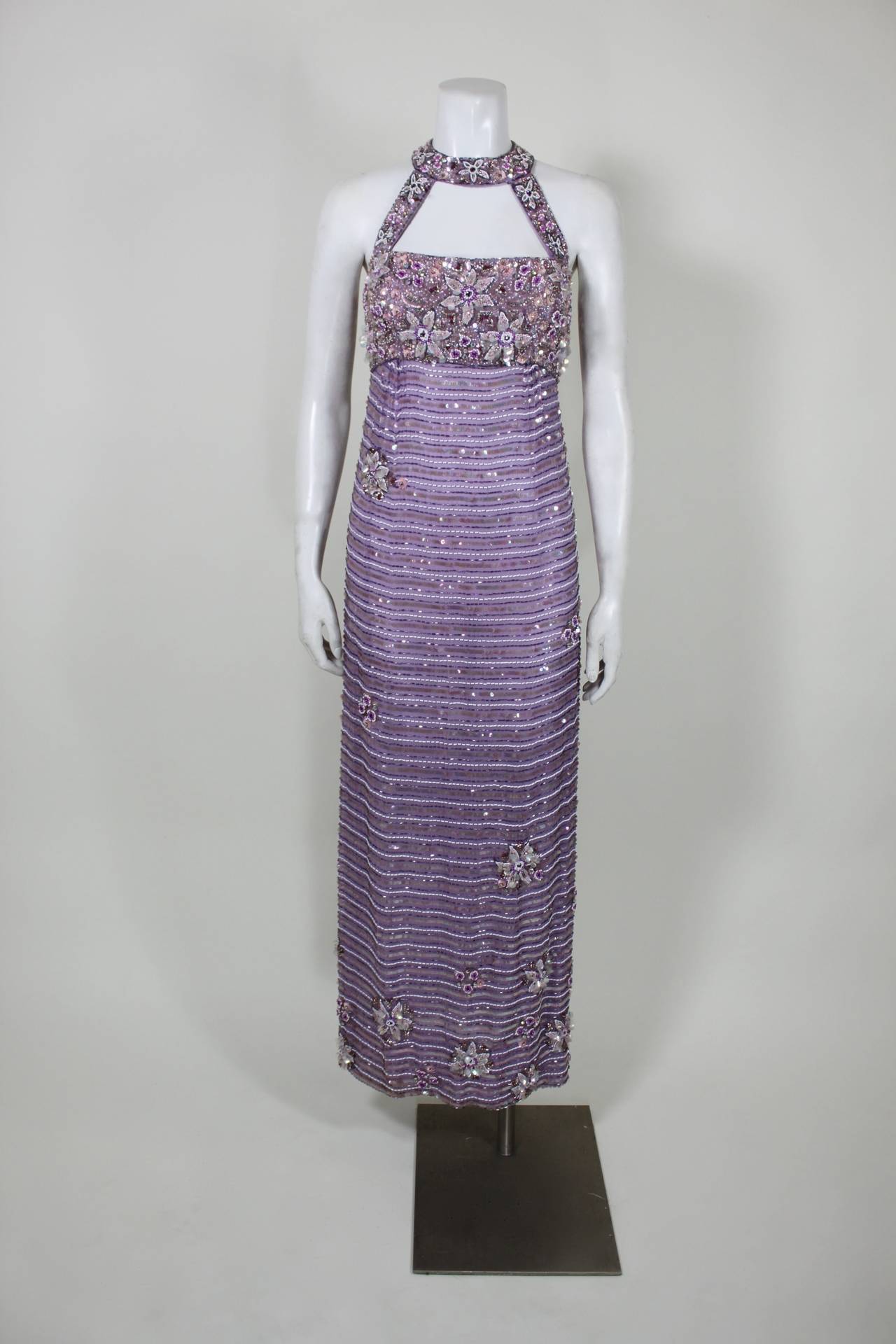 A show-stopping and sexy gown. A gorgeous shade of lavender is embellished throughout with dazzling bugle beads and sequins. The clusters of flowers feature iridescent paillettes and prong-set rhinestones. A classic column silhouette is given a