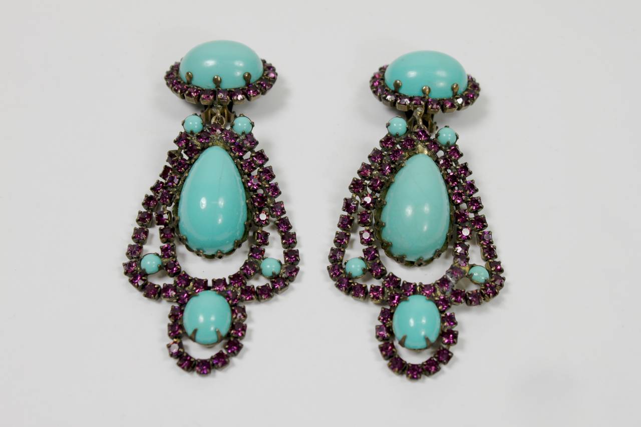 A pair of iconic earrings from Kenneth Jay Lane circa the 1960s. The earrings feature show-stopping faux turquoise pendants surrounded by dazzling plum rhinestones. Clip-on back.

